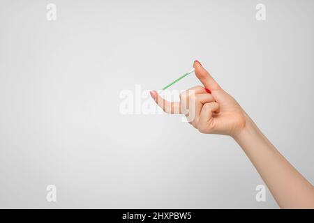 Ein Wattestäbchen zum Reinigen der Ohren in der Hand einer Frau mit rotem Nagellack. Stockfoto