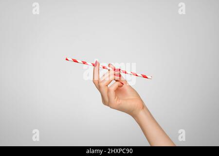 Ein helles Strohhalm für Getränke in der Hand einer Frau mit rotem Nagellack. Stockfoto