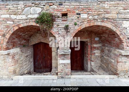 Gewölbter Eingang mit dicken mittelalterlichen Mauern zu einem Gebäude im Bagno Vignoni. Toskana, Italien Stockfoto