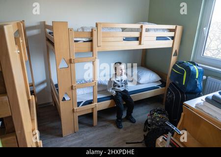 Barth, Deutschland. 14. März 2022. Lukas (6) sitzt auf einem Bett in einem Tierheim auf dem Gelände der Bernsteinreiter Barth-Erlebnisreitschule, nachdem er aus Lemberg geflohen ist. Der Junge floh mit seiner Mutter. Mehr als 20 Kriegsflüchtlinge sollen auf dem Gelände leben. Bisher haben mehr als eine Million Ukrainer ihre Heimat verlassen und sind zunächst in die Nachbarländer gegangen. Quelle: Stefan Sauer/dpa/Alamy Live News Stockfoto