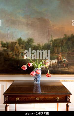 Rosa Tulpen in blau-weißer Vase auf Bidermeier-Tisch vor der riesigen alten Meister-Landschaftsmalerei Stockfoto