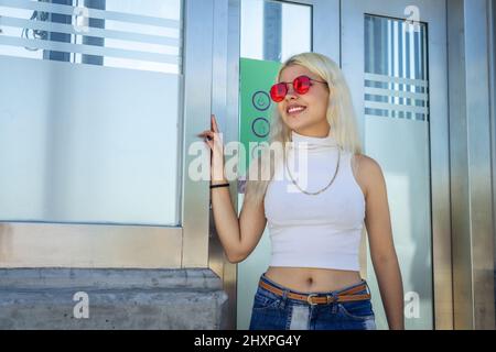 Junge lateinische Frau, die in der Tür eines verglasten Aufzugs auf der Straße steht. Copyspace. Stockfoto