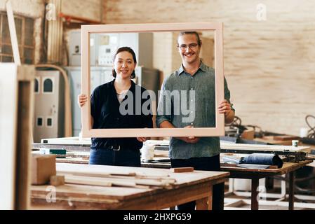 Waren immer bereit zu schaffen. Portrait von zwei jungen Zimmerleuten, die in ihrer Werkstatt einen Holzrahmen zusammenhalten. Stockfoto