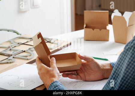 Männliche Hände halten eine Box in den Händen, Denkprozess auf Möglichkeiten, es zu verbessern. Hinter dem Schreibtisch sitzen. Kein Gesicht. Stockfoto