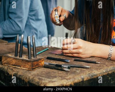 Menschliche Hände, die beim Handstempeln mit Hammer arbeiten oder Dekorationsmuster auf Metallplatte gravieren Stockfoto