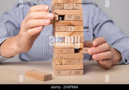 Planung, Risiko und Strategie im Geschäft. Holzblöcke Turm in Geschäftsleuten Hände Nahaufnahme. Mann nimmt Ziegel aus dem Stapel. Hochwertige Fotos Stockfoto