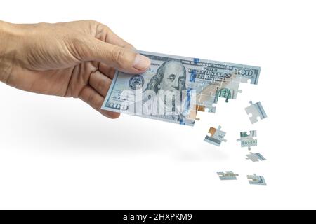 Männliche Hand mit einem 100-Dollar-Schein, der wie ein Puzzle zerfällt. Inflationskonzept. Stockfoto