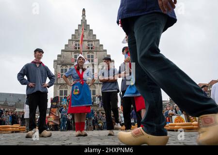 Mehrere Jungs, die die Käsesorten auf die Karren legen, sprechen mit Mädchen in traditionellen Kostümen vor dem alten Rathaus von Gouda Stockfoto