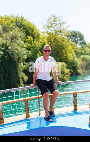 Ein Mann in einem weißen T-Shirt und Shorts steht und schaut an einem sonnigen Tag auf den türkisfarbenen Fluss Stockfoto