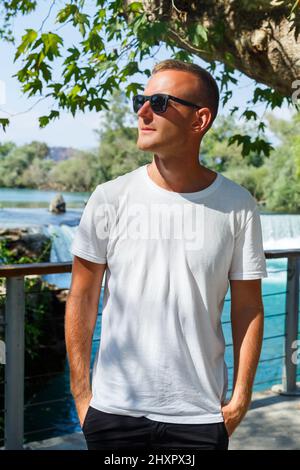 Ein Mann in einem weißen T-Shirt und Shorts steht und schaut an einem sonnigen Tag auf den türkisfarbenen Fluss Stockfoto