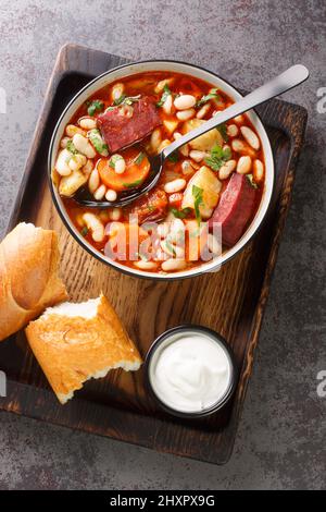 Traditionelle ungarische Babgulyas-Bohnen-Gulaschsuppe aus Pinto-Bohnen, geräuchertem Fleisch, Sellerie, Karotten in der Nähe auf dem Teller auf dem Holztablett Stockfoto