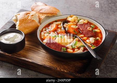 Babgulyas ist eine Gulyassuppe mit Bohnen, Fleisch, Sellerie, Karotten und Zwiebeln in der Nähe auf dem Teller auf dem Holztablett. Horizontal Stockfoto