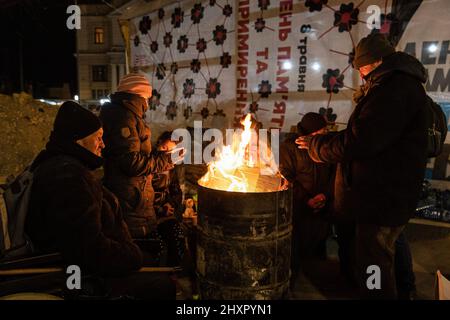 Lviv, Ukraine - 12. März 2022, Lviv, Ukraine. 12. März 2022. Ukrainer sitzen um das Feuer, um sich vor dem Bahnhof von Lemberg inmitten der russischen Invasion warm zu halten. Kredit: SOPA Images Limited/Alamy Live Nachrichten Stockfoto