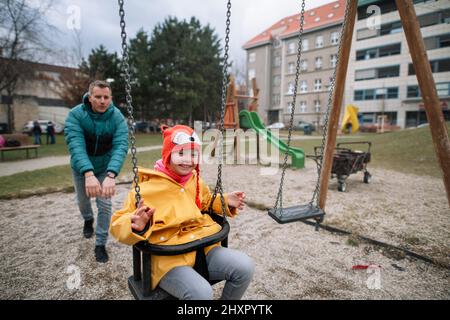 Vater schiebt seine kleine Tochter mit Down-Syndrom auf Schaukel im Freien auf dem Spielplatz. Stockfoto