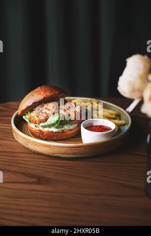 Falafel-Burger mit Salat, Tomaten, Zwiebeln, pommes frites, würzig duftender Sauce auf einem Holztisch. Vegetarisches Essen lecker und nahrhaft. Stockfoto