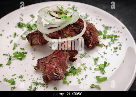 Gegrillte Lammrippchen mit Zwiebeln und Kräutern, auf dunklem Hintergrund Stockfoto