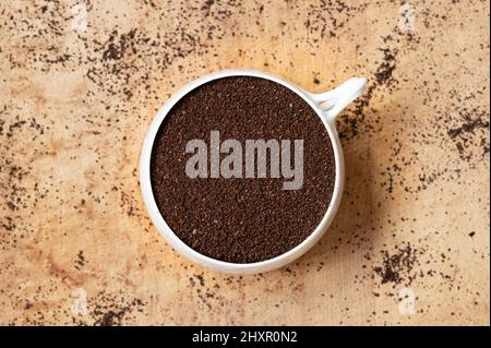 Blick von oben auf die weiße Kaffeetasse mit Kaffeesatz auf Holzhintergrund mit verstreuten Anlagen Stockfoto