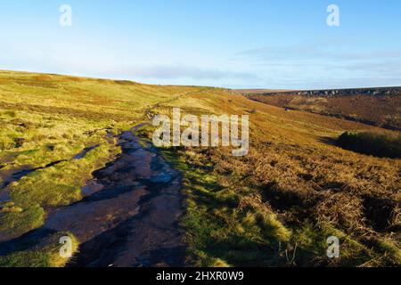 An einem sonnigen Herbsttag schlängelt sich ein feuchter, matschiger Pfad entlang der Hänge des Burbage Valley in Derbyshire. Stockfoto