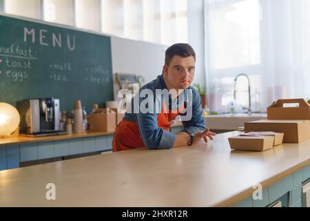 Young Down Syndrome Kellner, der im Take Away Restaurant arbeitet, Konzept der sozialen Eingliederung. Stockfoto