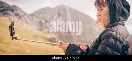 Wanderfrau, die ein Panoramabild der sommerlichen Berglandschaft fotografiert. Selfie-Fotostick. Zabljak Durmitor, Montenegro Stockfoto