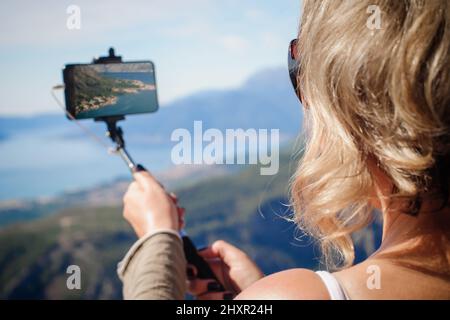 Schöne Frau, die ein Panoramabild der sommerlichen Berglandschaft fotografiert. Selfie-Fotostick. Zabljak Durmitor, Montenegro Stockfoto