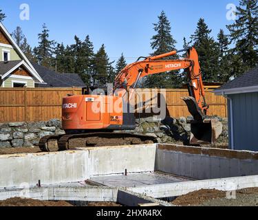 Ein Bagger, der hinter einem Zementfundament in einer neuen Unterabteilung arbeitet. Stockfoto