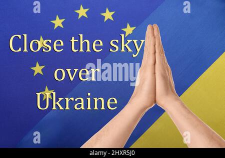 Hände von betenden Menschen und Texten SCHLIESSEN DEN HIMMEL ÜBER DER UKRAINE gegen Flaggen der EU und der Ukraine Stockfoto