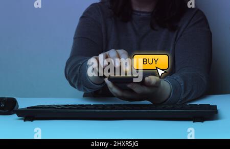 Frau, die über das Smartphone über die App einkauft. Hologramm-Bildschirm der Schaltfläche „Kaufen“. Mobiles Zahlungskonzept. Stockfoto