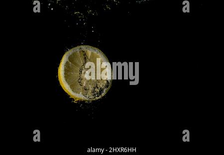 Frische Früchte fallen ins Wasser mit Spritzer auf schwarzem Hintergrund. Stockfoto