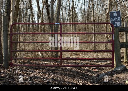 Alter roter Zaun im Park in der Nähe des Richtungszeichens, umgeben von Bäumen Stockfoto