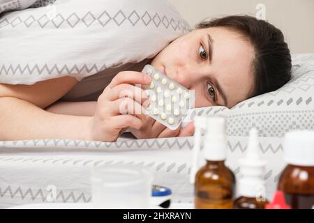 Eine kranke Frau liegt im Bett und hält Pillen in der Hand. Behandlung von viralen und bakteriellen Erkrankungen zu Hause Stockfoto