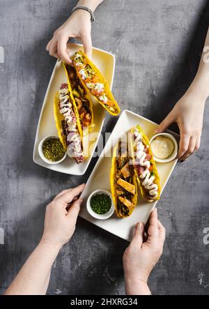 Set von Mais-Tacos mit Fisch und Fleisch auf einem Betontisch und weiblichen Händen. Zusammen essen Stockfoto