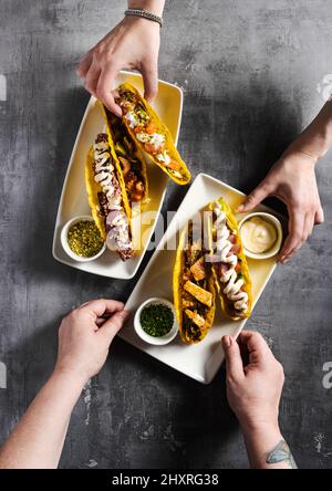 Set von Mais-Tacos mit Fisch und Fleisch auf einem Betontisch und weiblichen Händen. Zusammen essen Stockfoto