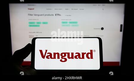 Person, die ein Mobiltelefon mit dem Logo des amerikanischen Finanzunternehmens The Vanguard Group Inc. Auf dem Bildschirm vor der Webseite hält. Konzentrieren Sie sich auf die Telefonanzeige. Stockfoto