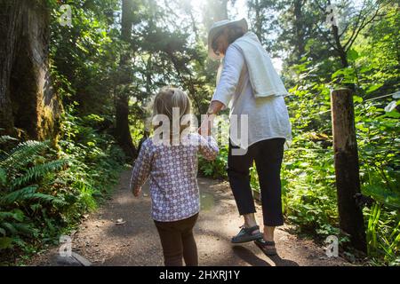 Eine Großmutter hält die Hand ihres Enkels auf dem Waldweg Stockfoto