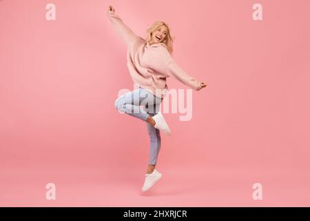 Fröhliche junge Dame, die springt, Spaß hat und lächelt, gut gelaunt ist und über rosa Hintergrund herumtöricht Stockfoto