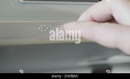 Nahaufnahme einer männlichen Hand, die Braille auf einem Metallschild berührt. HDR. Sehbehinderte oder blinde Person, die die Hand benutzt, um Informationen auf einem Metallschild zu lesen. Stockfoto