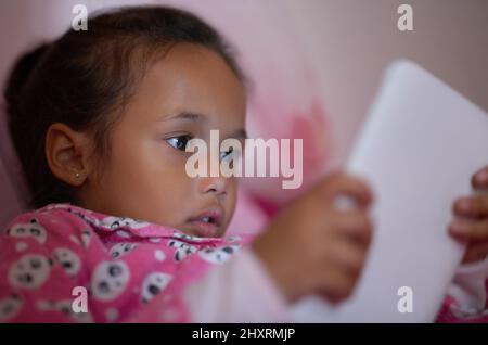 Shes ein neugieriges kleines. Aufnahme eines kleinen Mädchens, das mit einem digitalen Tablet im Bett liegt. Stockfoto