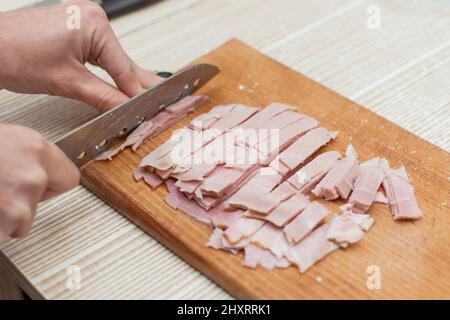 Frau schneidet Wurst, Schinken auf einem Schneidebrett. Stockfoto