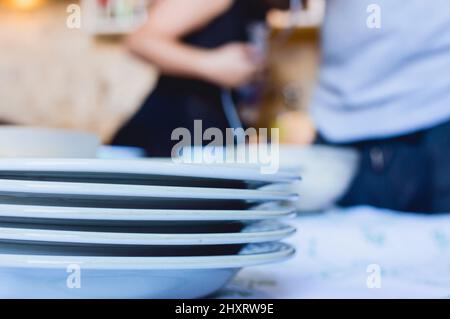 Weiße Porzellanteller auf einem Tisch mit verschwommenen Menschen im Hintergrund gestapelt Stockfoto