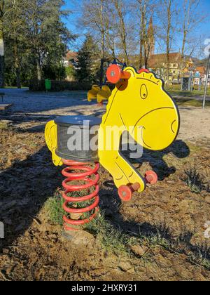 Frühling Wippe in Form eines stilisierten Pferdes auf einem leeren Kinderspielplatz mit Sandboden Stockfoto