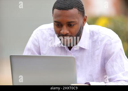 Ein hübscher Mann mit schwarzer Haut, der auf der Terrasse eines Cafés einen Laptop benutzt Stockfoto