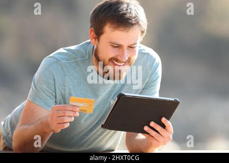 Glücklicher Mann, der online mit Kreditkarte und Tablet im Freien kauft Stockfoto