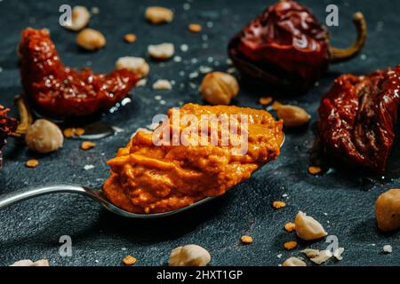 Nahaufnahme eines Löffels mit etwas Romesco-Sauce, typisch für Katalonien, Spanien, mit Tomaten, Knoblauch, Nyora Pfeffer, Haselnüsse und Olivenöl, auf einem dunklen Stockfoto