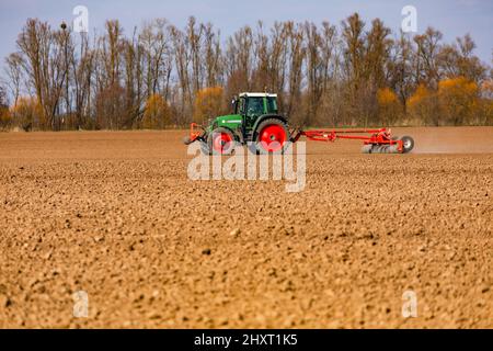 Im Hintergrund, vor einer Baumreihe, pflügt ein Bauer an einem sonnigen Wintertag mit einem Traktor ein Feld Stockfoto
