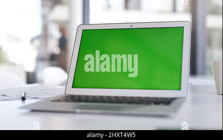 Achte darauf, dass deine Landing Page die lauteste Aussage macht. Aufnahme eines Laptops mit einem grünen Bildschirm auf einem Schreibtisch in einem modernen Büro. Stockfoto