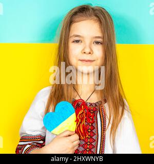 Ein Mädchen in einem nationalen ukrainischen Vyschywanka zeigt ein in Gelb- und Blautönen gemaltes Herz als Zeichen der Liebe zur Ukraine, Nahaufnahme gegen die Stockfoto