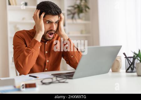 Schockiert arabischen Kerl greifen Kopf mit Laptop Stockfoto