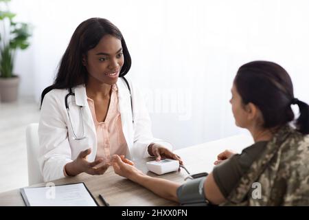 Schwarze Ärztin, Die Weibliche Soldatin Berät Und Ihren Blutdruck Überprüft Stockfoto