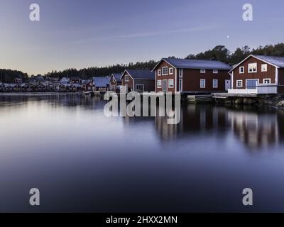 Schöne Aussicht auf hölzerne rote Häuser in der Nähe eines Sees mit Reflexion im Wasser in Bonhamn, Schweden Stockfoto
